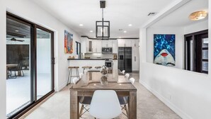 A modern kitchen with white cabinets, a central island, and a dining area with a glass table and white chairs.
