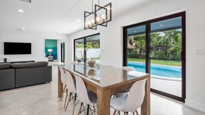 A modern kitchen with a large island, a dining area with a glass table, and a view of a swimming pool.
