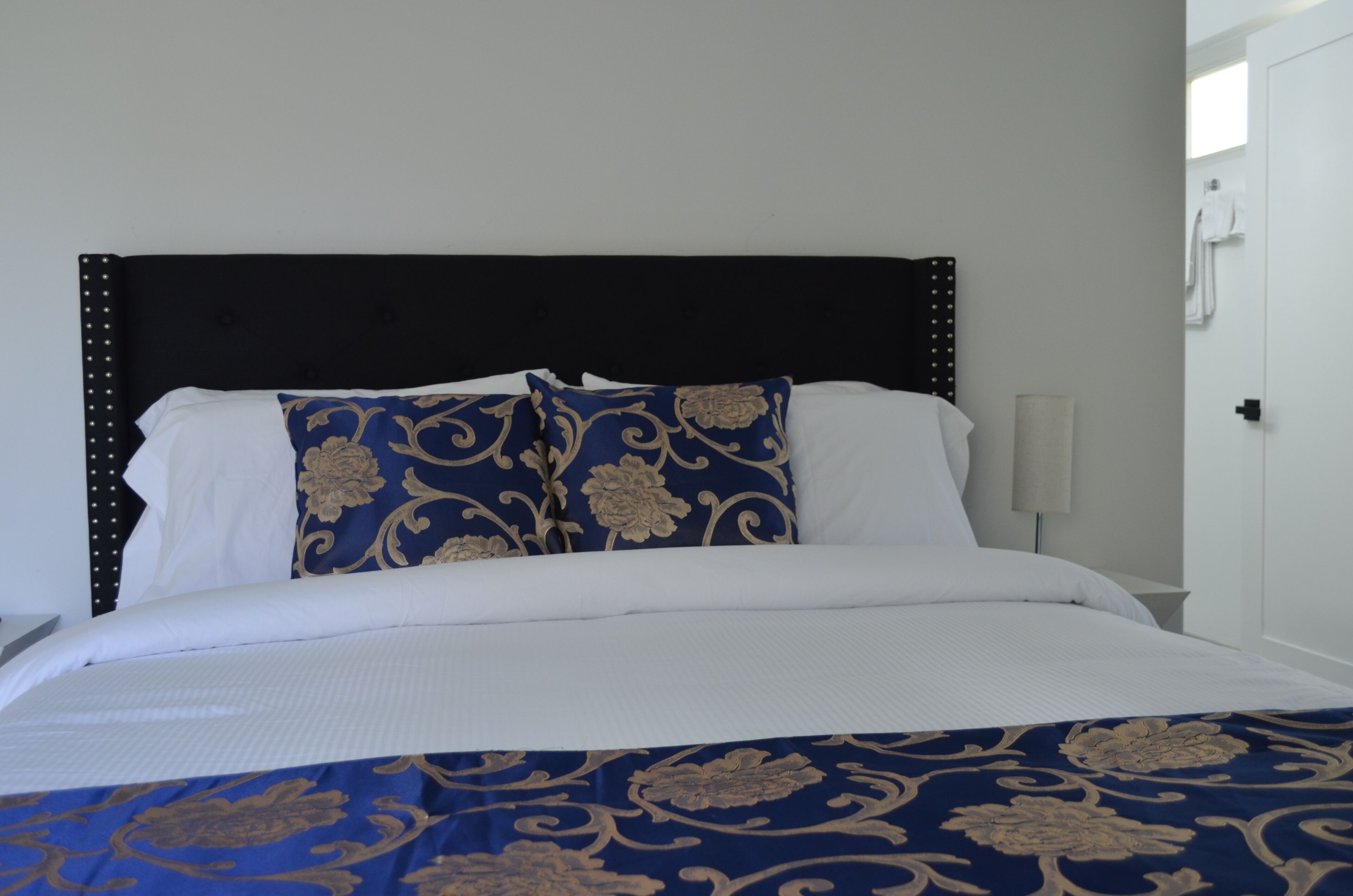 A neatly made bed with a dark headboard, white linens, and blue and gold patterned pillows.