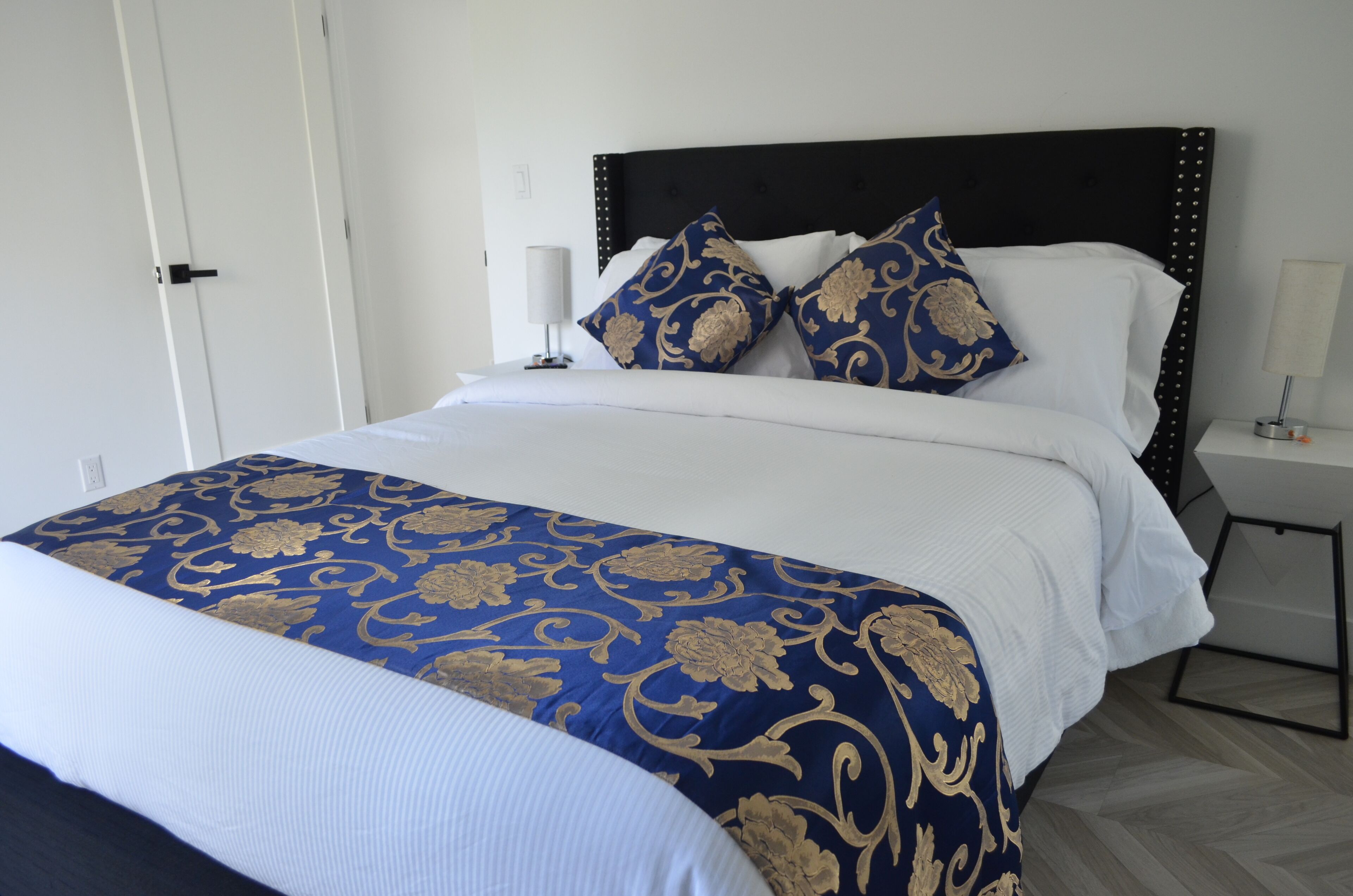 A neatly made bed with a blue and gold patterned bedspread, white pillows, and a dark headboard.