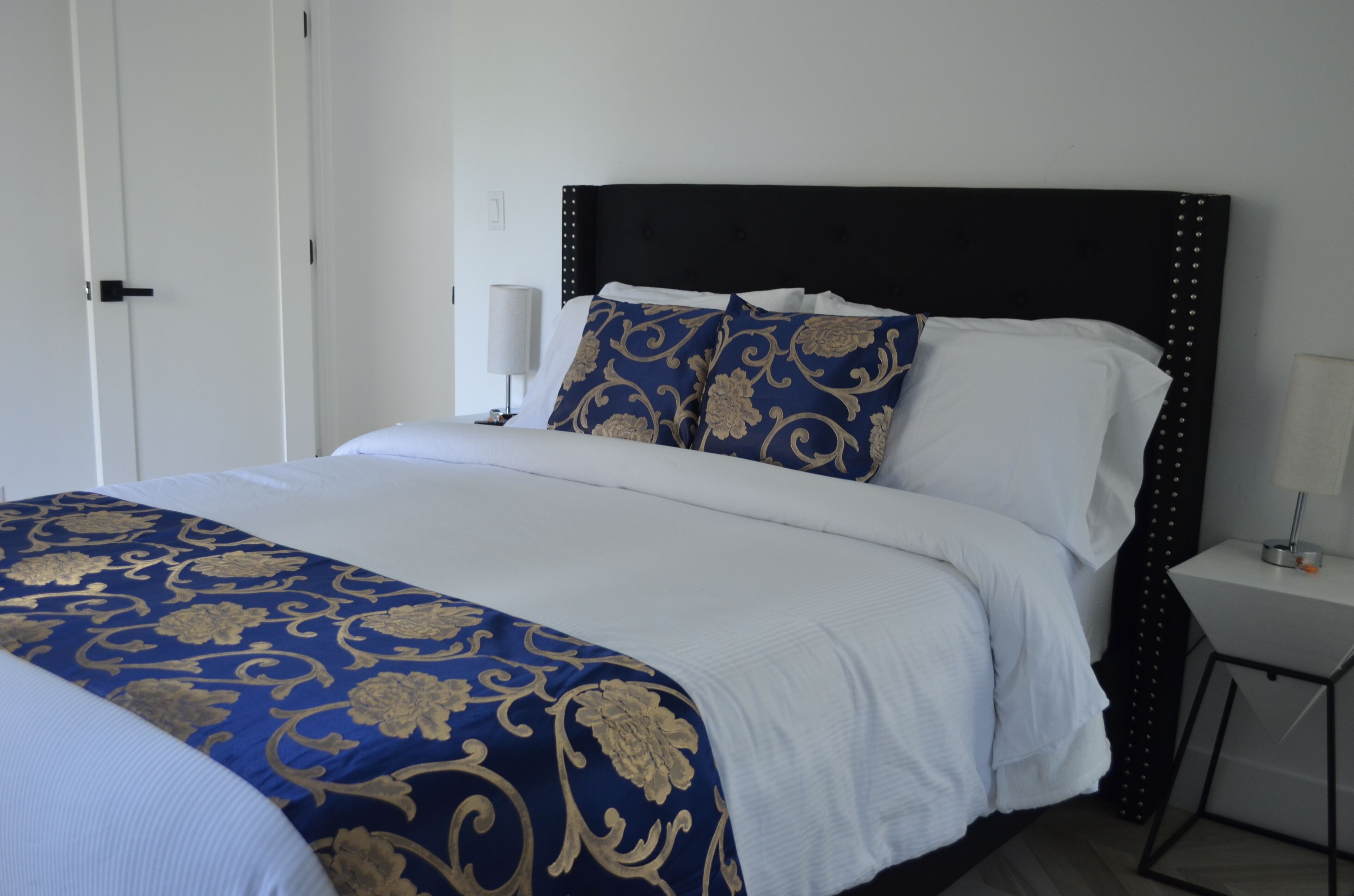 A neatly made bed with a blue and gold patterned bedspread, white pillows, and a black headboard with decorative studs.