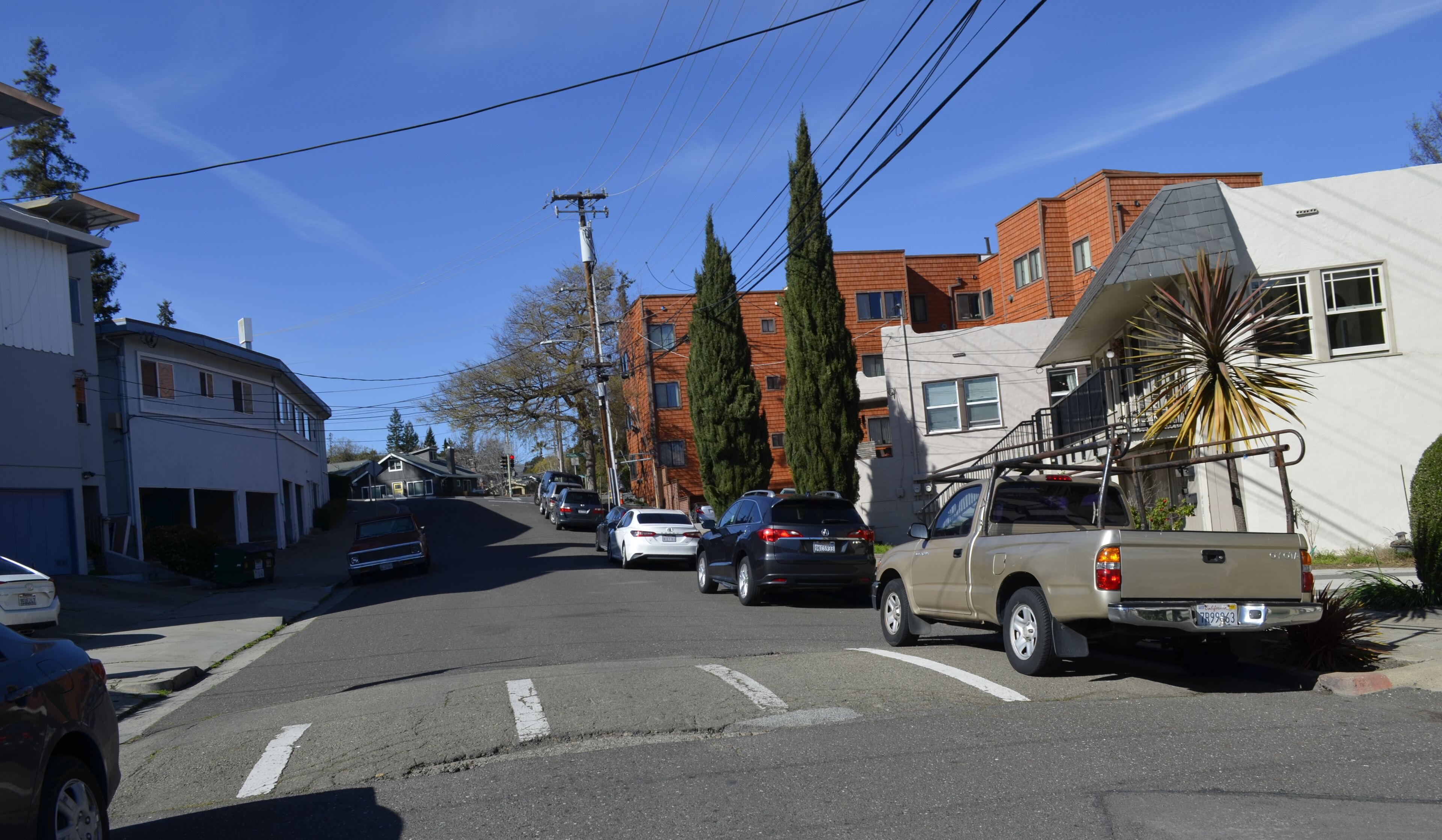 A residential street with houses, parked cars, and a clear blue sky.