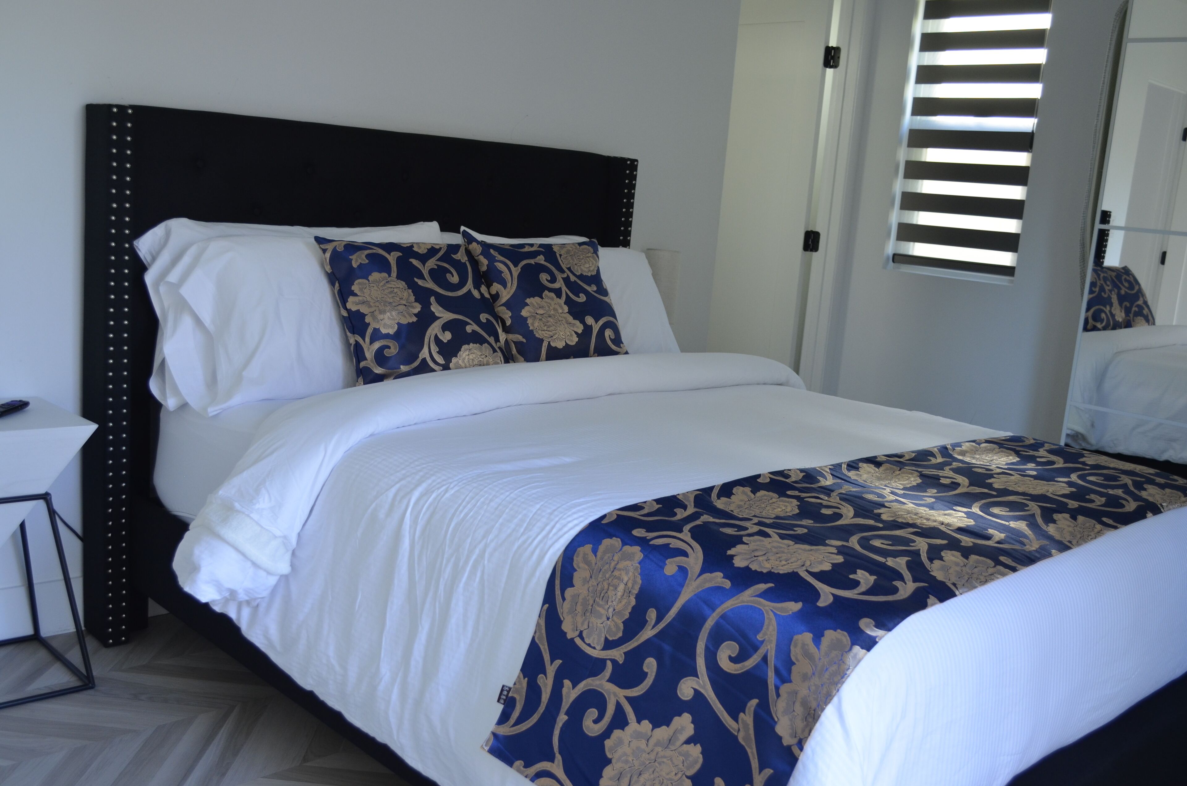A neatly made bed with a dark headboard, white bedding, and a blue and gold patterned throw blanket.