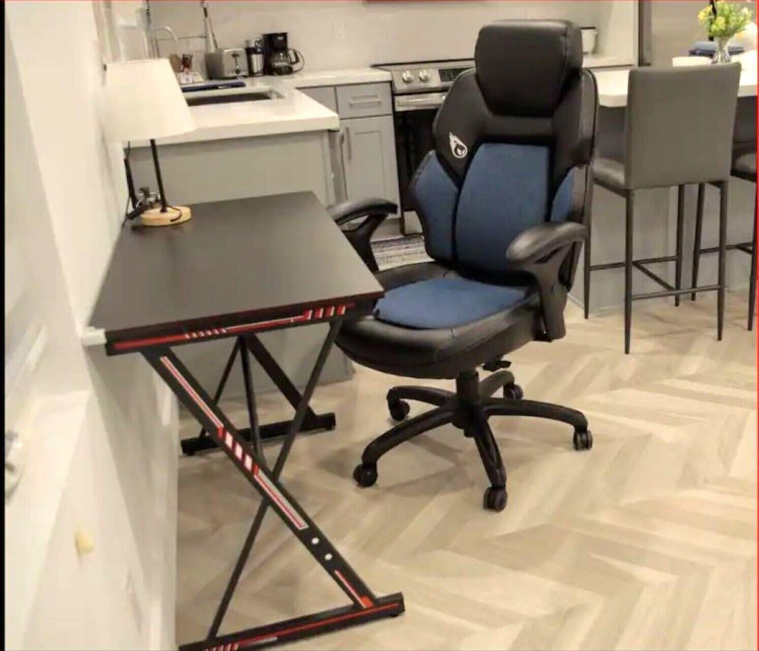 A modern kitchen with a black and blue office chair, a small dining table, and a coffee machine.