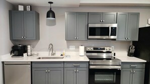 A modern kitchen with grey cabinets, a stainless steel sink, a coffee maker, a microwave, an oven, and a dishwasher. - Golf Close to lakes. 2 bedroom, 2 bath. Sleeps 6 Pool. (Mancelona)