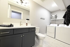 Un baño moderno con un lavamanos blanco, gabinetes oscuros, un inodoro y dos secadores blancos.