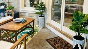 Een gezellig hoekje met een houten tafel en stoelen, een bloempot en uitzicht door een groot raam.