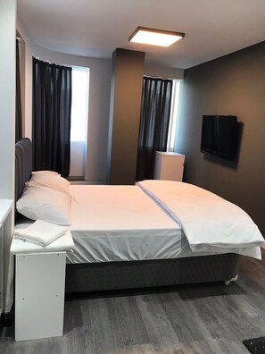 Une chambre d’hôtel moderne dotée d’un grand lit, d’un bureau et d’un téléviseur à écran plat fixé au mur.
