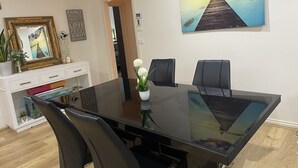 Un espace repas moderne avec une table en verre, des chaises noires et un tableau représentant une jetée.