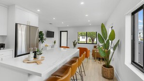 A modern kitchen with a large island, white cabinetry, and a flat-screen TV. - Modern Miami Home- 5 min from Coral Gables & Coconut Grove, 15 min from Brickell (Miami)