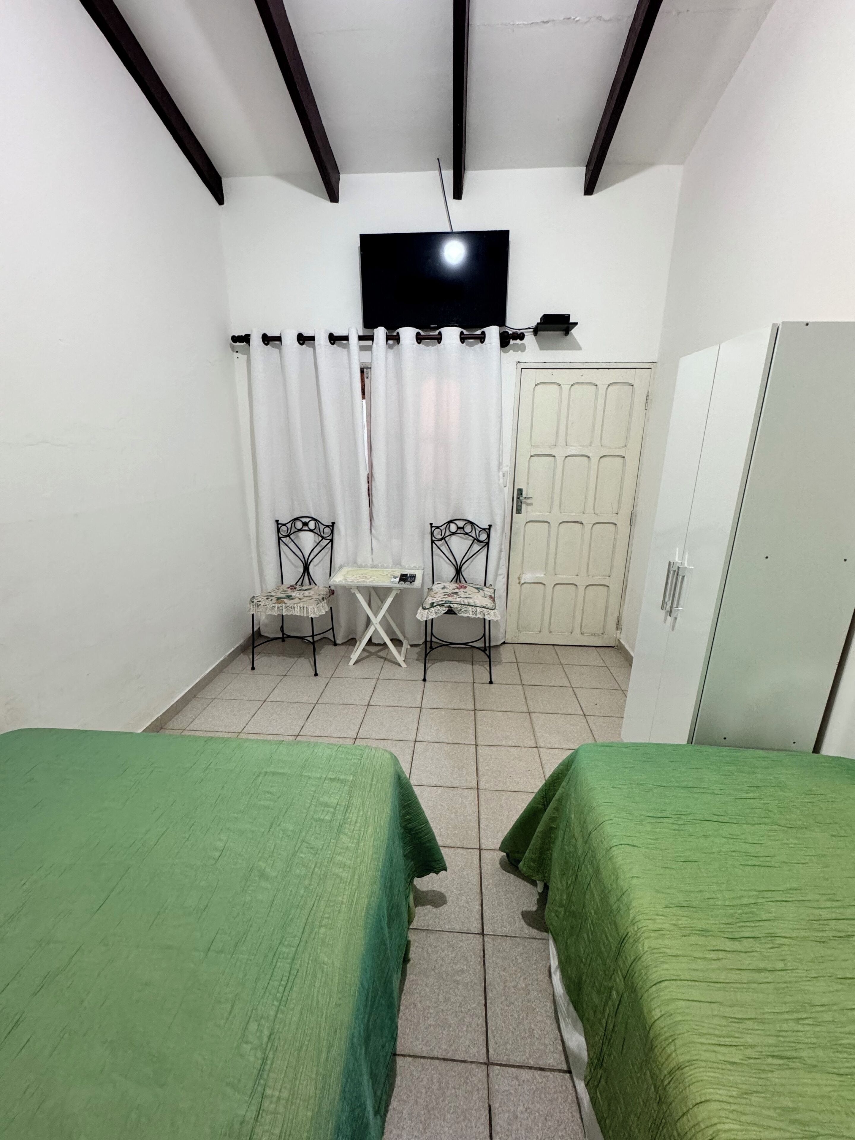 A small room with two beds, a TV, a table, two chairs, and a wardrobe.
