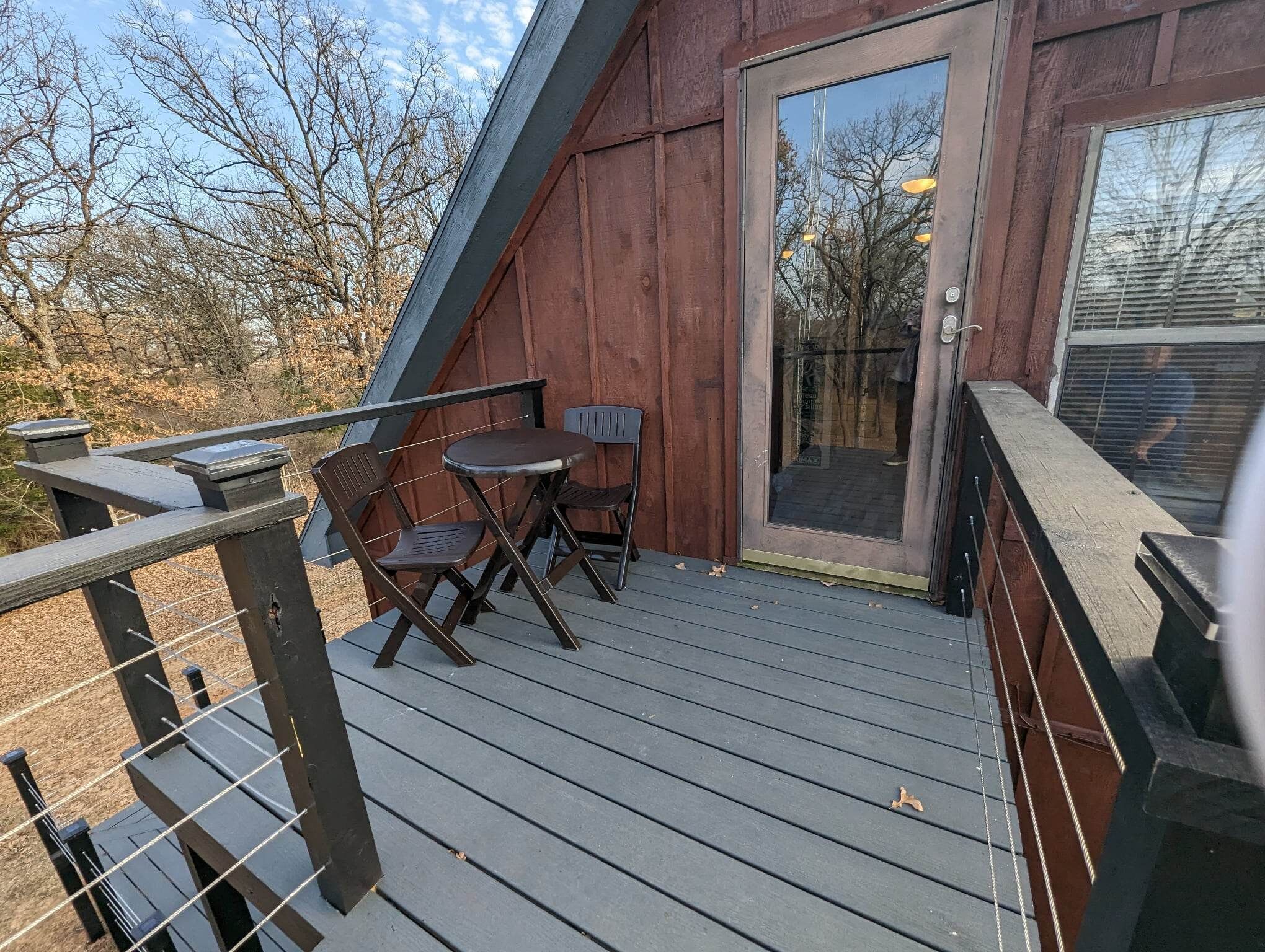Une terrasse en bois avec une porte vitrée donnant sur un espace abrité, deux chaises et une petite table.