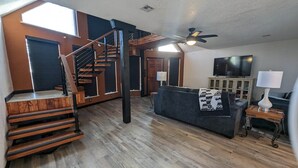 Ein geräumiges Wohnzimmer mit Holzboden, einer Wendeltreppe, einem Deckenventilator, einem Sofa, einem Fernseher und einer Lampe.