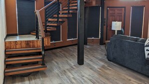 Un interior moderno con una escalera de madera, un sofá y una puerta con una lámpara.
