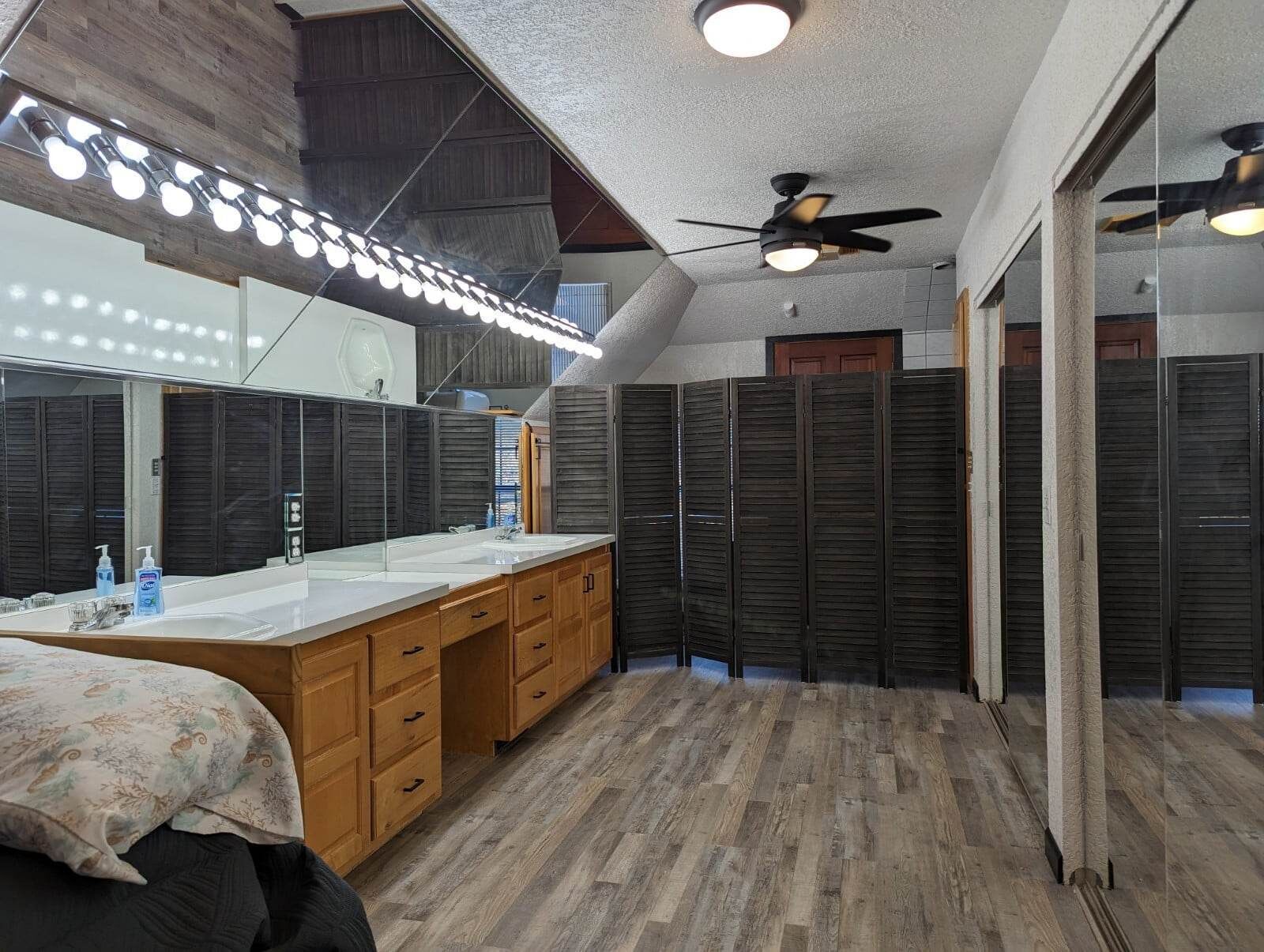 A modern bathroom with a large mirror, vanity, wooden cabinets, and a ceiling fan.