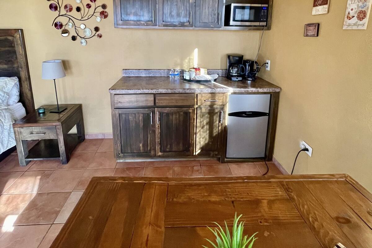 A compact kitchen with wooden cabinets, a microwave, a coffee maker, and a small refrigerator.