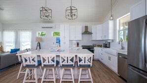 Una cocina moderna con armarios blancos, una isla central con taburetes de bar, electrodomésticos de acero inoxidable e iluminación colgante.