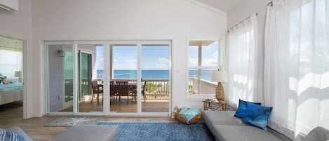 A spacious living room with a large gray sofa, a blue rug, and a view of the ocean through large windows.