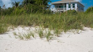 Una casa de playa con balcón, rodeada de hierba alta y arena.