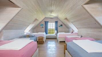 Ein gemütliches Schlafzimmer im Dachgeschoss mit Holzbalken an der Decke, zwei Betten mit rosa und blauer Bettwäsche, einem Fenster mit blauen Vorhängen und einem kleinen Stuhl.