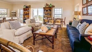 A spacious living room with a high ceiling, a fireplace, and a view of the outdoors. There are multiple seating areas with sofas and chairs, and a coffee table in the center. - Buccaneer Hill Main House 5 Bedroom Home (Governor's Harbour)