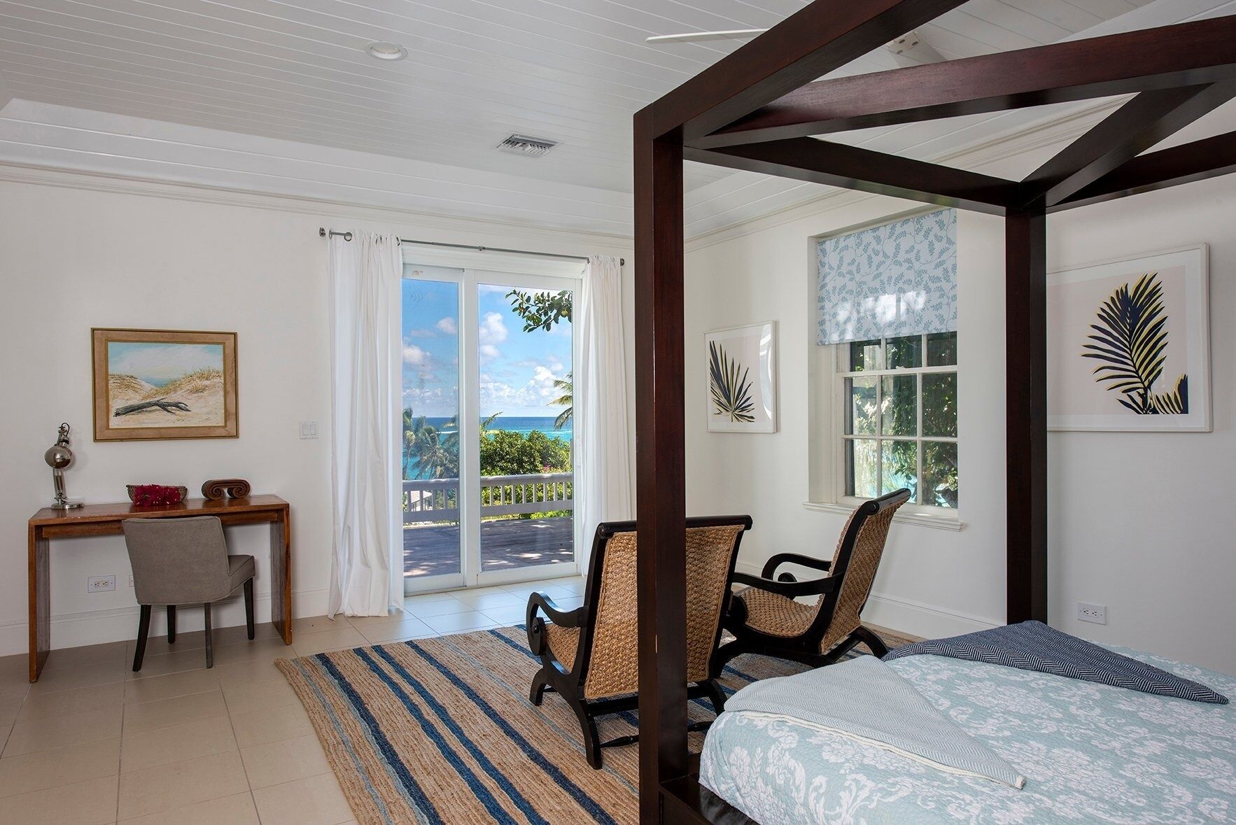 A bedroom with a bed, two chairs, a desk, and a view of the ocean.