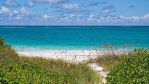 Ein Strand mit klarem türkisblauem Wasser, weißem Sand und grüner Vegetation.