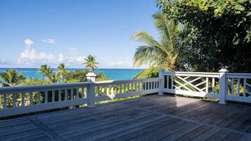A wooden deck with a white railing overlooking a beach with palm trees and the ocean.