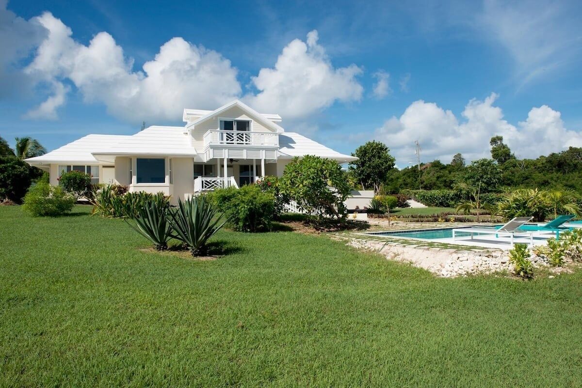A large white house with a balcony, surrounded by a well-maintained lawn and a swimming pool.