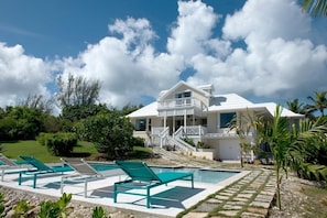Ein modernes Haus mit Pool, umgeben von viel Grün und blauem Himmel.