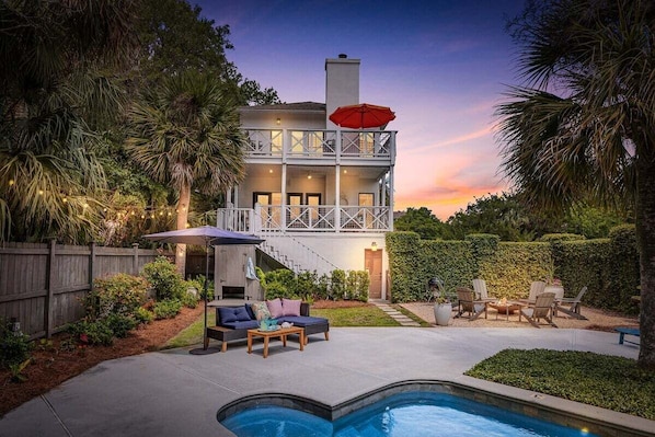 Una casa de dos pisos con balcón, piscina y mobiliario de exterior.