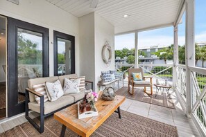 A spacious balcony with a sofa, a wooden table, and a chair. - Beautiful home w/ private pool near Coast Cottage (Saint Simons Island)