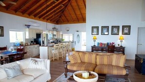 A spacious living area with a high ceiling, a kitchen in the background, and a dining area with a table and chairs.