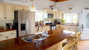 A kitchen with wooden countertops, a stainless steel refrigerator, a microwave, and a sink.