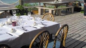 A wooden deck with a table set for dining, overlooking a clear blue sea.