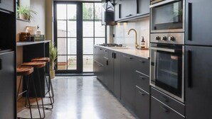 A modern kitchen with dark cabinetry, stainless steel appliances, and a bar area with stools. - The Old Fish Bar (Margate)