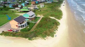 Uma área residencial à beira-mar, com casas perto da praia, destacando-se uma casa com varanda, e uma praia arenosa.