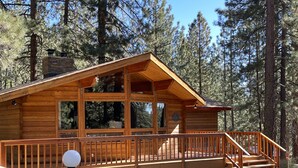 Une cabane en bois dotée d’une terrasse, de grandes fenêtres et d’une cheminée en pierre.