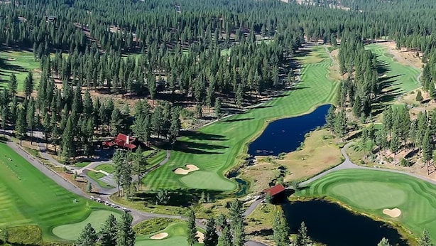 Une vue aérienne d’un parcours de golf comportant plusieurs trous, entouré de forêts denses et bordé d’un lac.