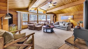 L’intérieur chaleureux d’un chalet avec des murs en bois, une cheminée, une grande fenêtre et un coin salon confortable.
