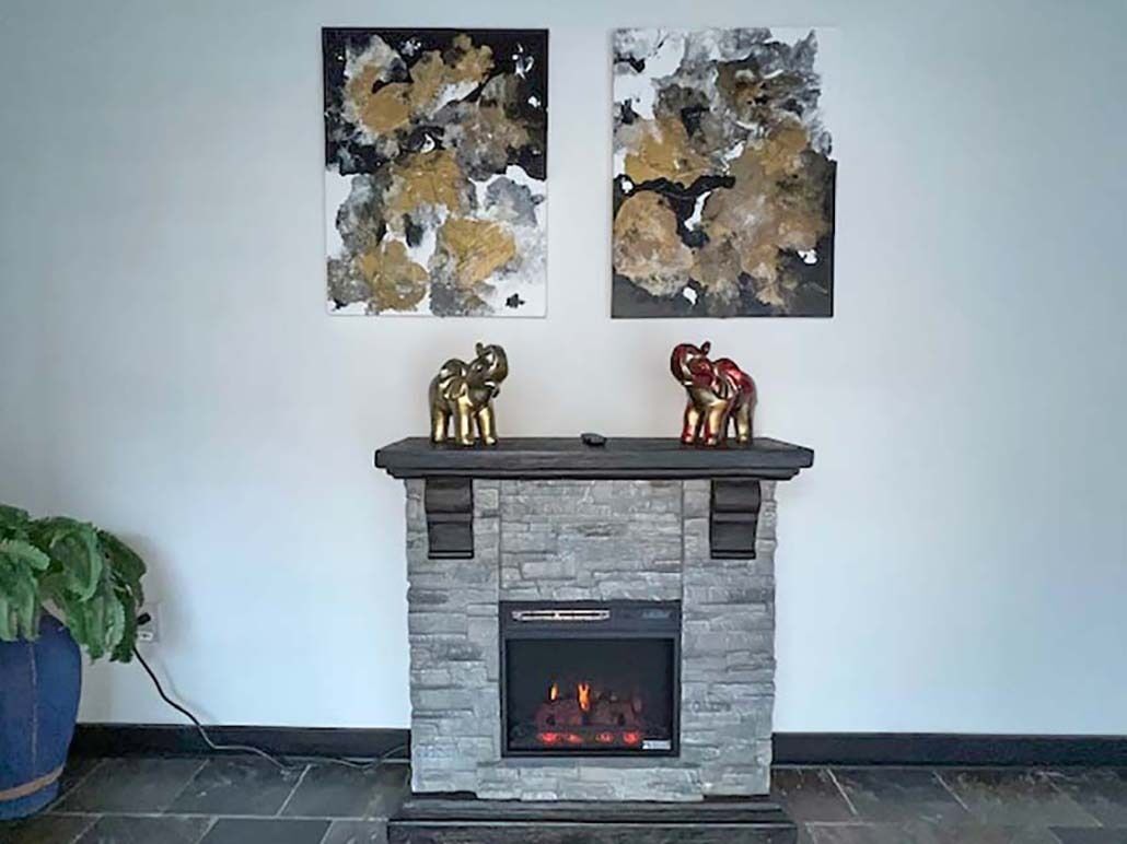A fireplace with a stone facade and two abstract paintings above it.