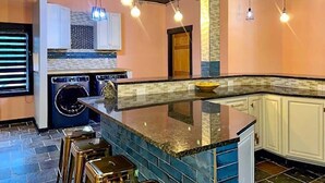 Une cuisine moderne dotée d’un plan de travail en granit, d’appareils électroménagers intégrés et de luminaires suspendus.