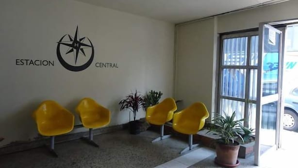 Un área de espera con un letrero de brújula en la pared, varias sillas amarillas y plantas en macetas.