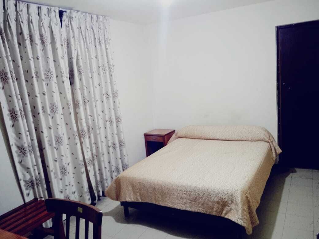 Una camera da letto con un letto, una sedia in legno, un comodino di legno e una tenda con motivo floreale.