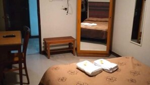 Habitación de hotel con cama, escritorio, silla, televisor y espejo.