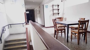 Un pasillo de hotel con una escalera, sillas de madera y una mesa.