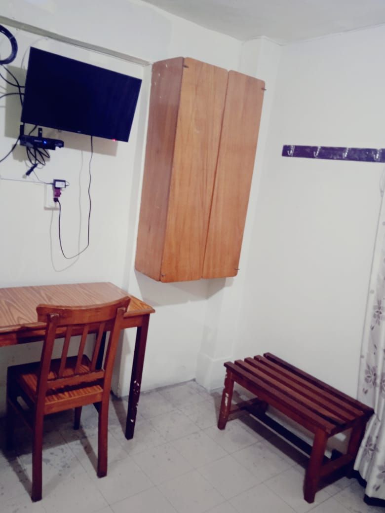 A room with a wooden table and chairs, a television mounted on the wall, and a wooden cabinet.