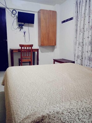 Un dormitorio con una cama, un escritorio de madera, una silla, un televisor montado en la pared y un armario.