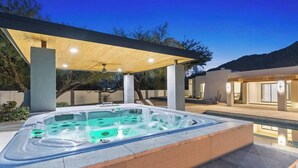 Un bain à remous sous une pergola en bois, avec une piscine en arrière-plan.