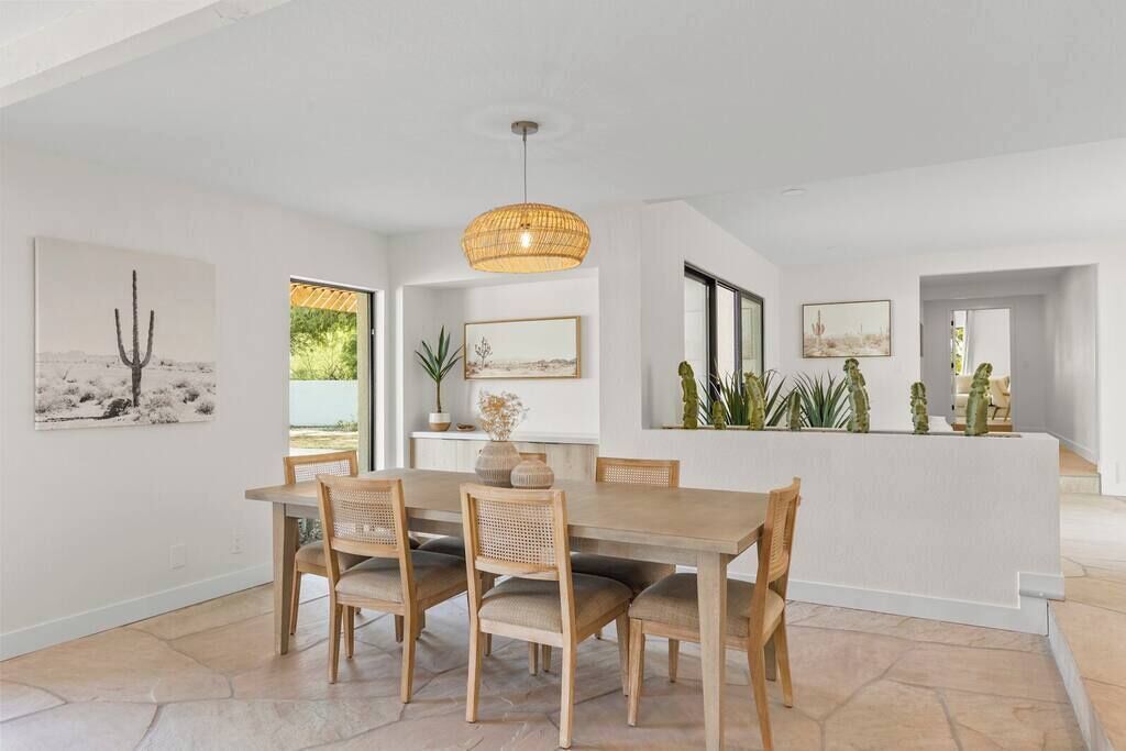 A dining area with a wooden table and chairs, a hanging light fixture, and framed artwork on the walls.